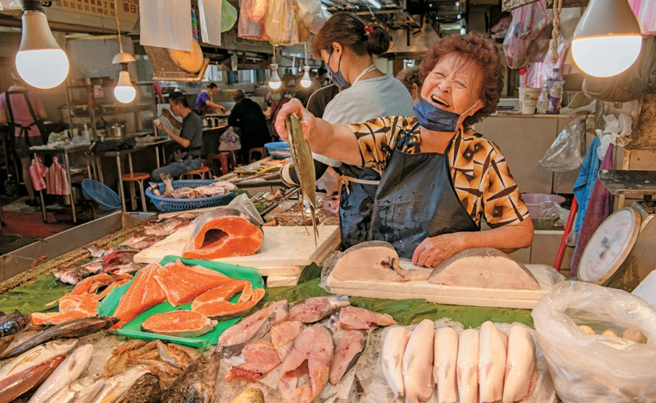 热情招呼客人的海鲜摊老板娘，拿起鲜鱼展现对自家商品的自信。（摄影／李智为）