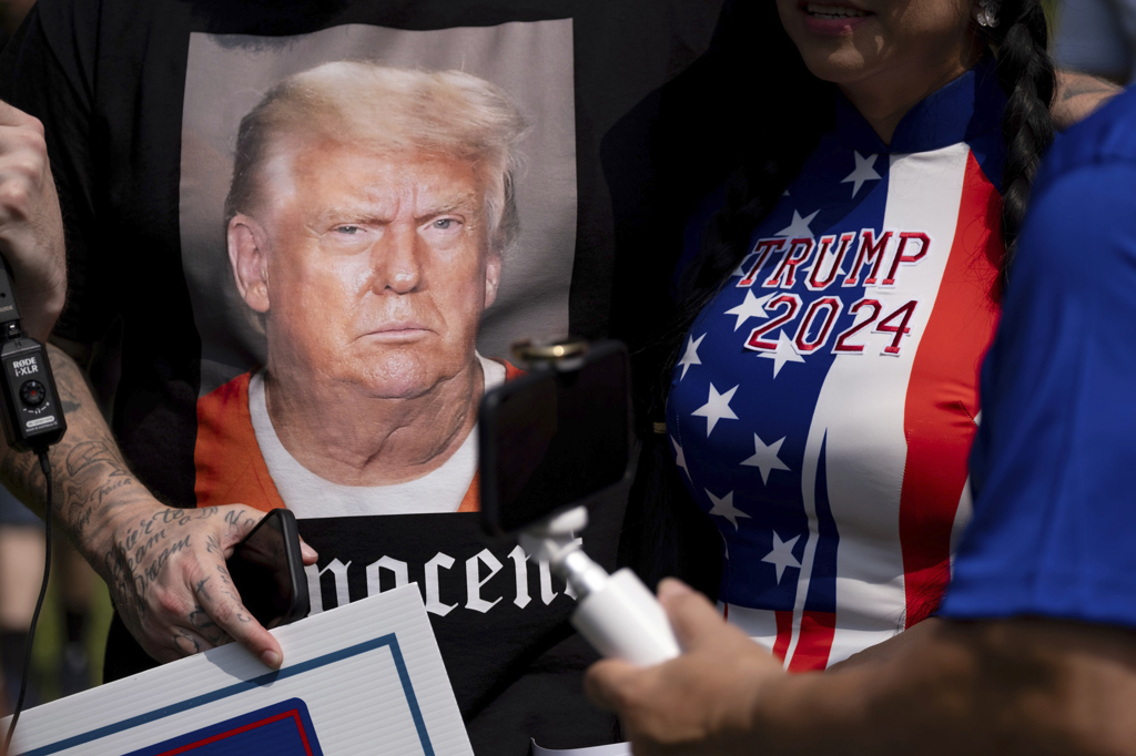 川普24日赴乔治亚州富尔顿郡监狱到案并拍摄档案照，支持者持印有川普照片的T恤与竞选旗帜在监狱外守候。（美联社）(photo:ChinaTimes)