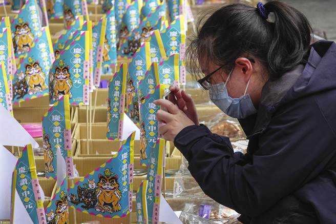 一名女子拿起供品仔细检视或拍照。（黄子明摄）