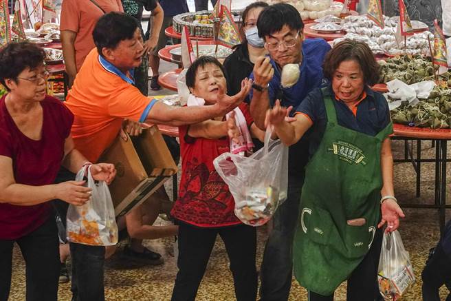 民眾与志工争抢道长分享的供品。（黄子明摄）