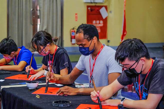 竹縣去年舉辦首屆縣長盃全國書法大賽，來自美國非裔的Thomson「唐海澤」（右二），高大身形，低頭書寫，展現書法藝術不受國界、年齡的限制 。（羅浚濱攝）