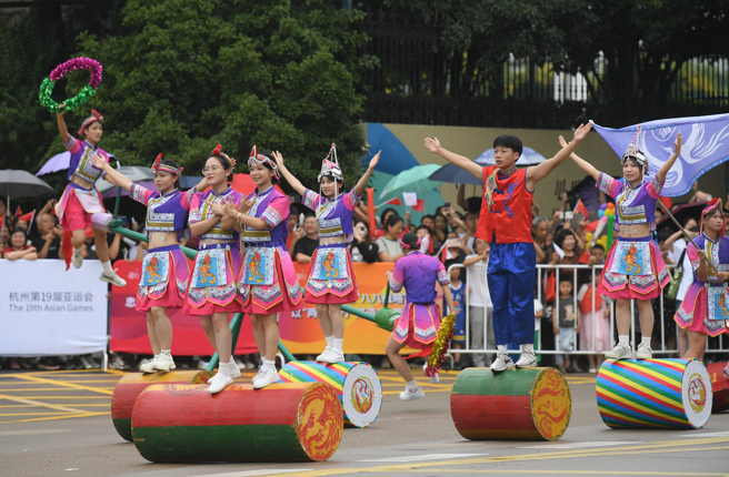 身着民族服饰的演员在圣火传递下沿线表演。（新华社）