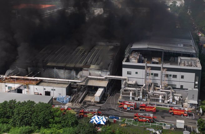 屏东科技产业园区明扬高尔夫球厂22日发生爆炸，火场23日持续闷烧，上午10时浓烟转为更加浓烈，一旁的厂房岌岌可危，多部消防车在旁待命，消防人员在两间厂房间狭窄通道灌水降温。（黄子明摄）