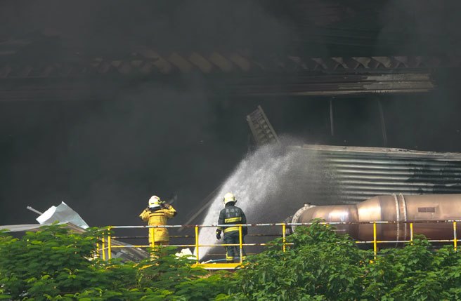 屏东科技产业园区明扬高尔夫球厂22日发生爆炸，火场23日持续闷烧，上午10时浓烟转为更加浓烈，消防人员不断灌水降温。（黄子明摄）