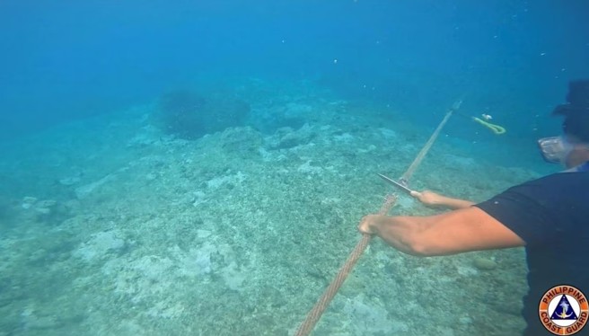 一张未注明日期的照片，菲律宾海岸警卫队人员切断了黄岩岛附近安装的浮动屏障绳索。(图/路透社)