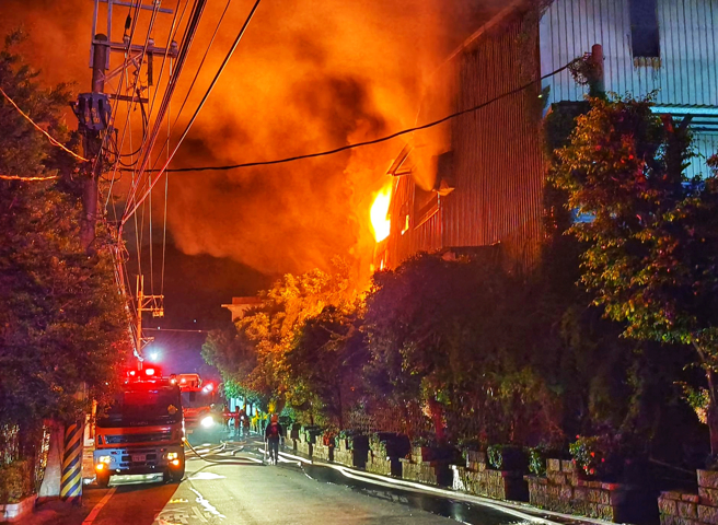 八里废五金回收场厂暗夜大火 ，大批警消忙射水灌救，铁皮厂房全面燃烧剩骨架 。(黄世麒摄)