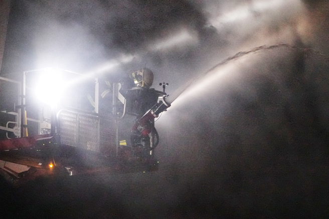 八里废五金回收场厂暗夜大火 ，大批警消忙射水灌救，铁皮厂房全面燃烧剩骨架 。(黄世麒摄)