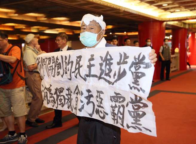 魏耀乾（中）在民进党37周年创党党员餐会拉布条抗议。（中时资料照，张铠乙摄）