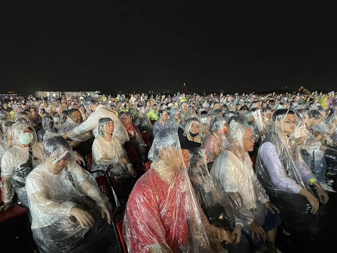 台南空军基地8日晚间登场的国庆晚会下起滂沱大雨，现场有搭游览车前来的民眾，因无法离开，无奈穿雨衣坐在露天的观眾席。（程炳璋摄）