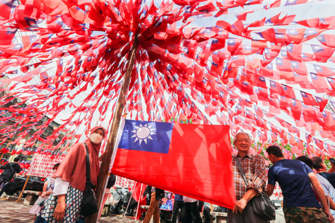 庆祝国庆日，滇缅游击队孤军后裔张老旺第29年自发性在龙冈举行升旗典礼，国旗屋升旗已成桃园龙冈地区国庆日传统，今年移师中坜龙江市民活动中心举行，周边挂满1.8万面国旗，旗海飘扬十分壮观，参加民眾在升旗后与国旗合影。（资料照／陈麒全摄）