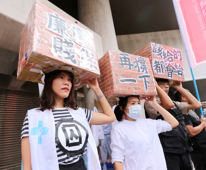 台湾医疗工会联合会将于22日举办「地狱职场嘉年华，医疗劳权大游行」活动。主办单位12日在立法院前召开行前说明记者会，表示台湾血汗医疗早已不是新闻，医疗人员忍耐到了极限，各种光怪陆离、不合理的事物，彷佛活在如同地狱般的职场，强调医疗人员大量离职、出走，已成为严重的国安问题。成员们顶着写有「廉价贱保」、「再撑一下」、「该给的都会给」的大砖头，讽刺医疗人员薪资待遇不佳、劳动权益低落。（黄世麒摄）