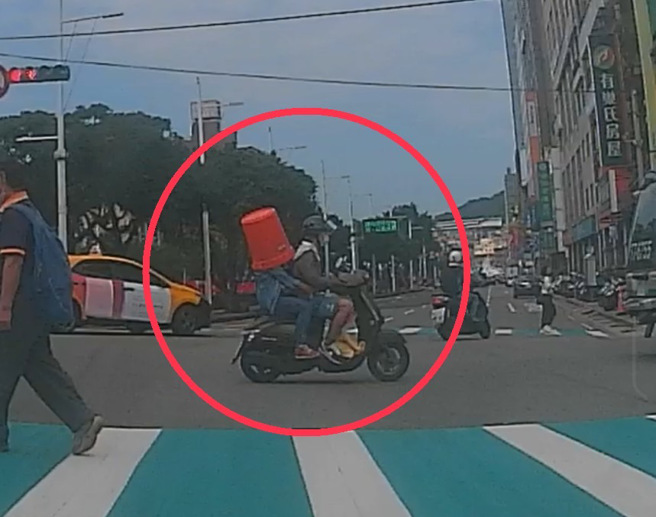 基隆市一名网友昨日突见前方一名骑士后座的乘客，头套橘色大水桶，全程忘我地穿梭于道路，后将此一幕拍下，上传至脸书社团：「今天上班路上遇到的奇景」。（图 / 民眾授权提供）