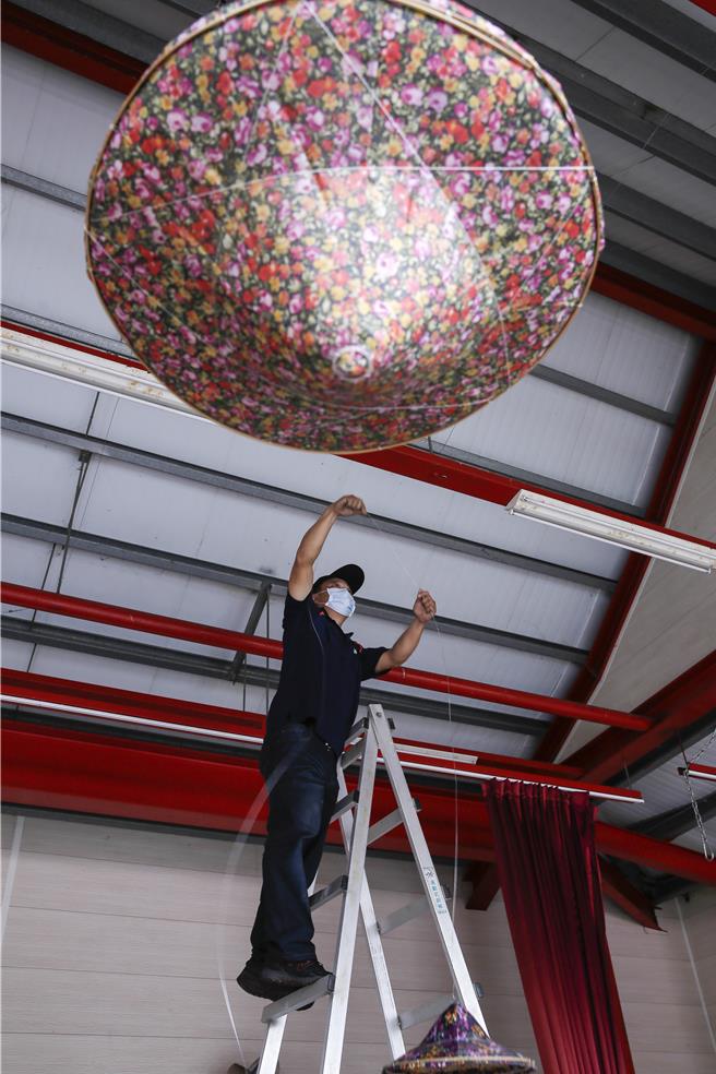 獅潭鄉新店社區27日在義民廟舉辦打新丁粄活動，28日有敬拜天神儀式與八音配樂、戲曲班等表演，以及生態體驗及農特產品展售，志工們正在戲台上布置套上客家花布的斗笠。（黃子明攝）