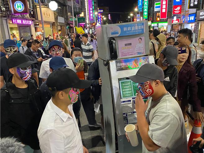 「新政治提款機」人裝道具今晚7點參加萬聖大遊行時準時，多名臉譜人圍在一旁，其中1人還不時抽菸。（陳育賢）