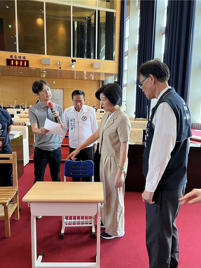 台中市议员江肇国(左)等人质询时将课桌椅搬到议事堂内，要求副市长王育敏(右二)体验、坐坐看。(林欣仪摄)