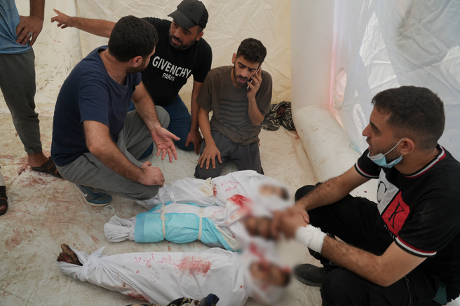 2023年10月24日阿克薩醫院，3個男子和親戚的父親站在以色列轟炸遇難的巴勒斯坦兒童屍體旁。（美聯社）