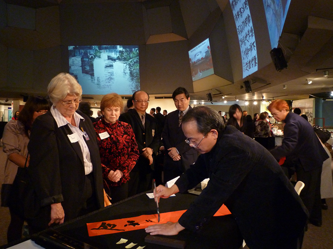 2010年时任臺中市长胡志强（左四）与副市长、时任文化局长黄国荣（左五）率队赴德州文化中心举办「大墩美展」，艺术家现场挥毫赠墨宝。（图片来源：臺中市政府文化局提供）