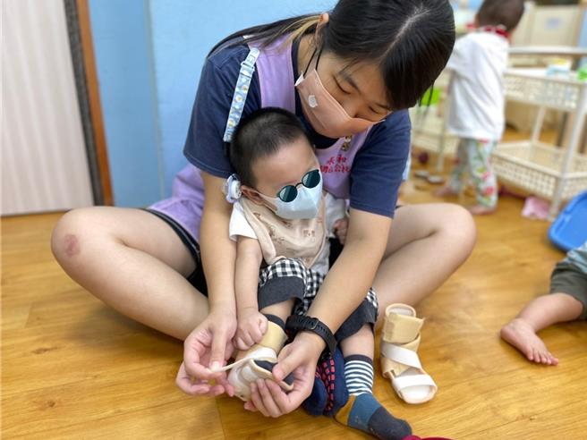 Apple老师陈雨晴细心帮球球穿上踝足辅具。（新北市社会局提供）