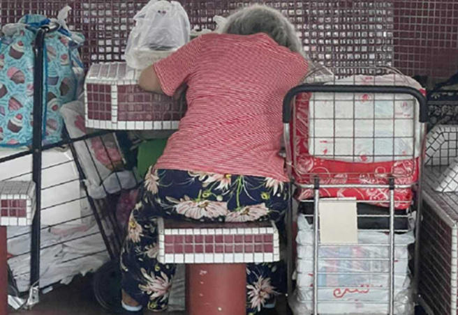 该名妇人在石桌椅处就地趴着休息，一旁可见3辆手推车上堆满行李袋、塑胶袋等生活用品。（图 / 翻摄画面）