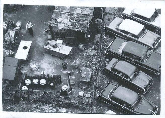 一九六○年代的臺北館前路街角一景，富裕與貧窮僅一牆之隔，和當時西方的柏林圍牆，以及東方韓國三十八度線，頗有異曲同工之妙。（圍牆內外，1965年，黃伯驥攝／台北市立文獻館提供）