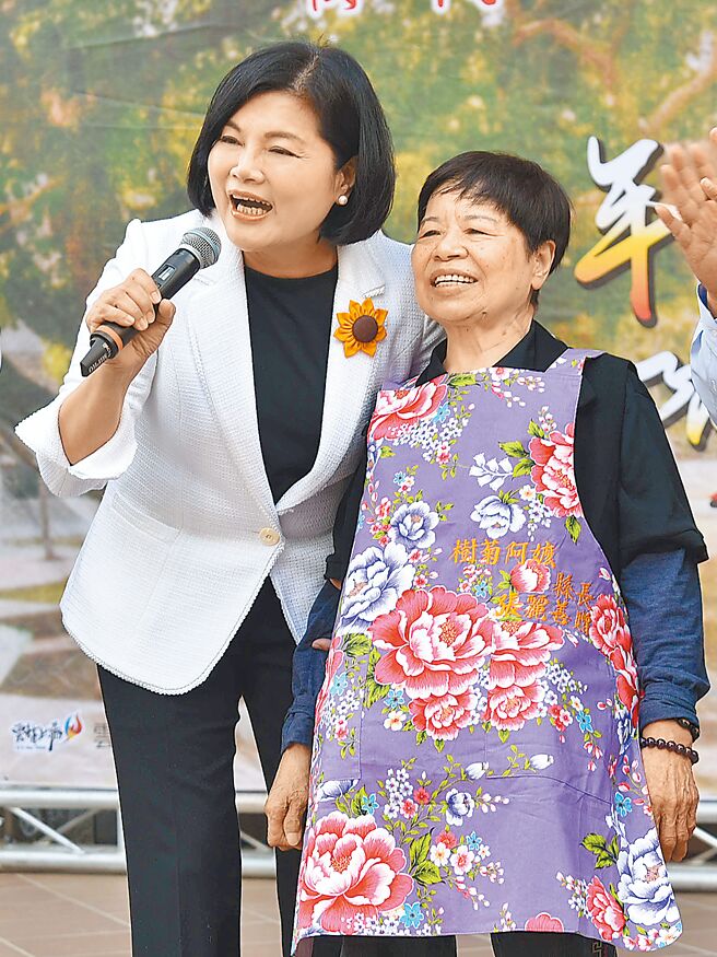 菜贩陈树菊（右）获得第一届荣耀云林典范奖，19日在斗六市镇西国小对小朋友分享心得，县长张丽善（左）为她围上围裙，让小朋友回想品德教科书上那个阿嬷。（云林县政府提供／周丽兰云林传真）