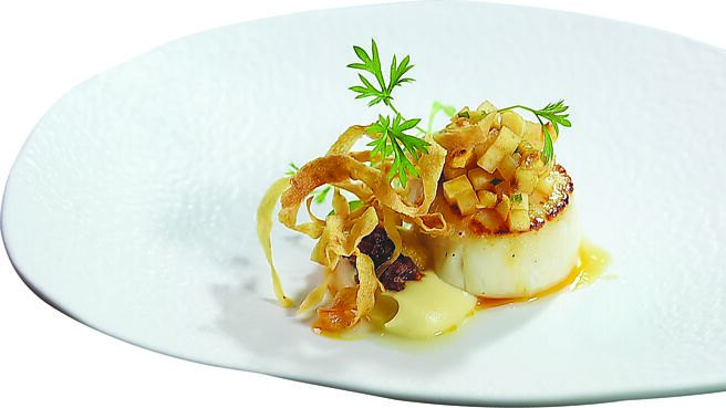 〈嫩煎北海道干贝〉是将饱满肥厚的干贝煎到五分熟，搭配滑顺的防风根泥、腌渍大头菜榛果莎莎，上方点缀烤过的西班牙腊肠及酥炸防风根脆片，一起食用，口感与味觉层次丰富。图／姚舜