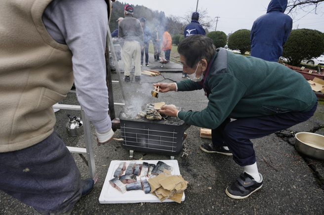 石川县珠洲市地震灾区一处临时设置的避难所，3日有志工在路边架起炉灶烘烤鱼肉供灾民充飢。（美联社）