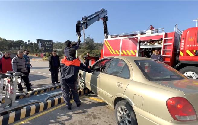 金門男子為送友人趕搭小三通船班，疑似在轉彎時因車速過快，直接「騎上」水頭港臨時停車格旁之路沿石，導致整輛車卡在上面動彈不得，消防隊只能出動吊臂車前來救援。(圖／民眾提供)