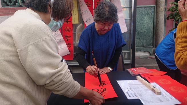 台南市延平國中退休校長洪麗里（中）寫春聯50年，27日在大觀音亭參加春聯揮毫，舉龍年春聯民俗禁忌，提醒有龍圖形春聯勿貼進室內。（程炳璋攝）