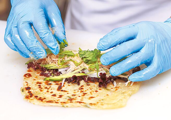 4.蔥油餅鋪平，中間位置依序鋪上生菜、洋蔥絲、紅蘿蔔絲、小黃瓜絲、東坡肉、香菜，最後撒上花生粉。（粘耿豪攝）