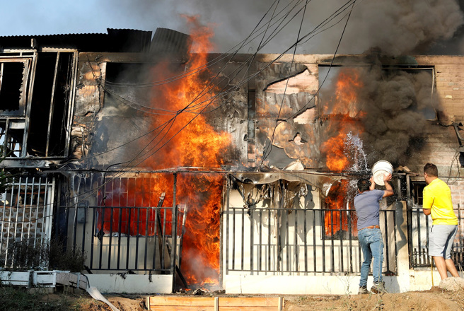 智利中部沿海觀光城鎮比納薩瑪（Vina del Mar）一棟民房被野火吞噬，居民急忙救火。（圖／路透社）