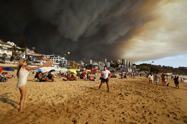 畫面為民眾2日在智利中部沿海觀光城鎮比納薩瑪（Vina del Mar）海灘玩耍，附近森林野火引發的濃重煙霧籠罩天際。（圖／美聯社）