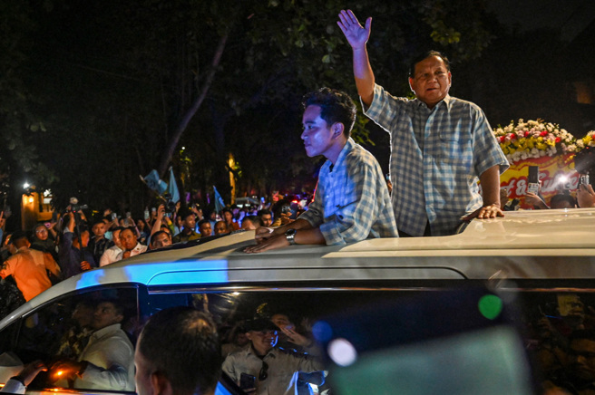 印尼总统参选人、国防部长普拉伯沃、副总统候选人吉伯朗（现任总统佐科威长子）14日在车上对支持者挥手。（路透社）