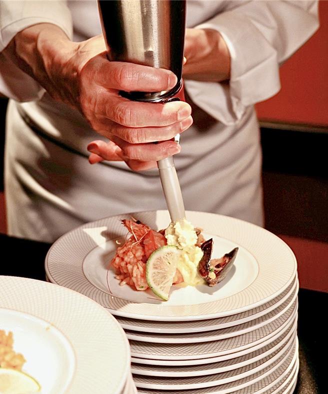 师傅挤上慕斯酱搭配西班牙腊肠海鲜饭，是限定的敲锣美食。（台北远东香格里拉提供）