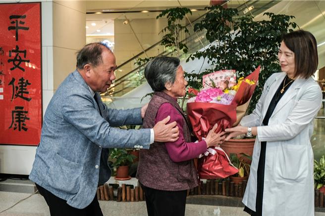 中医大新竹附医外科部长沈名吟（右）获认证达文西机器手臂手术观摩中心女医师，96岁的许廖阿嬷（中）坚持离开轮椅上前献花给沈，其子（左）则现身说法，场面感人。（罗浚滨摄）