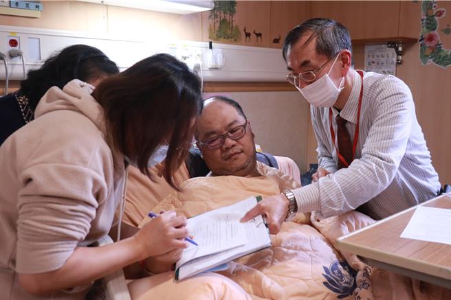 台灣腦庫代表人台大醫院醫師謝松蒼（右）解說後，無法執筆的黃鼎承由太太協助握筆，簽屬捐贈同意書。（台中慈濟醫院提供）