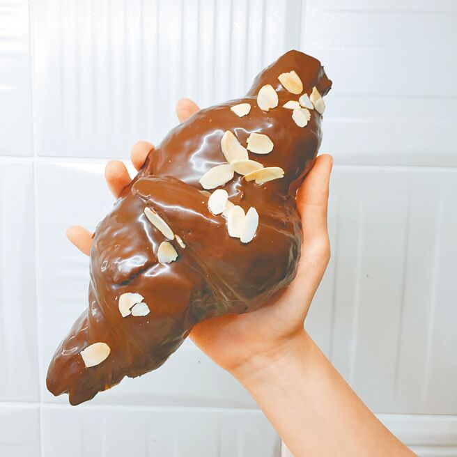 成人手掌般大的「巧克力牛角」，超過15公分的酥脆可頌裹上香濃巧克力醬和杏仁片，期間限定45元。（普諾麵包坊忠孝店提供）