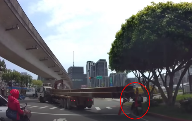 有驾驶拍到1辆拖板车因载着过长钢梁，导致左转弯时K到路边停等红灯的骑士。（图／ 翻摄自「WoWtchout-地图型行车影像分享平台」）