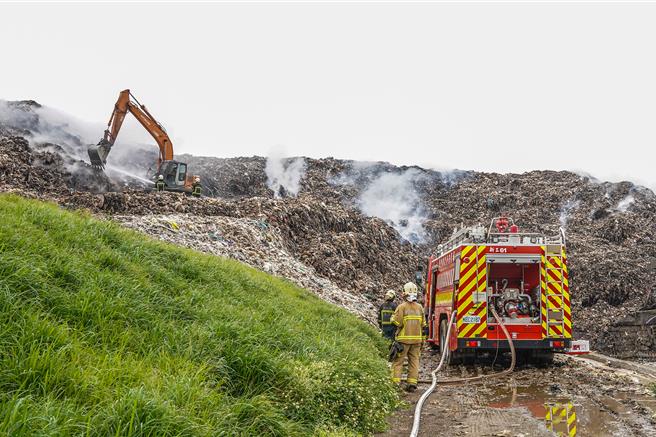 新竹县新丰垃圾掩埋场发生沼气引发的自燃火警，6日火势扑灭后仍处于闷烧状态，现场调派怪手将堆置垃圾挖开，希望能降温，避免火势復燃。（罗浚滨摄）