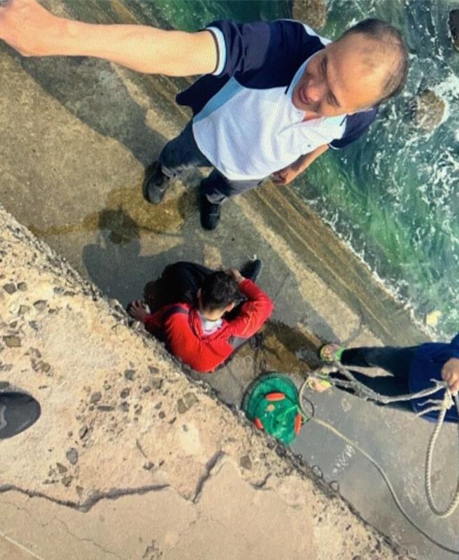 2024年4月10日澎湖縣／澎湖西嶼合界碼頭一名釣客（紅衣者）6日耍帥拍照不慎落海，只能緊抱消波塊待援，竹灣派出所所長林輝雄（左）獲報後趕往，利用現地漁船用纜（右）將釣客套住救起。（警方提供／許逸民澎湖傳真）