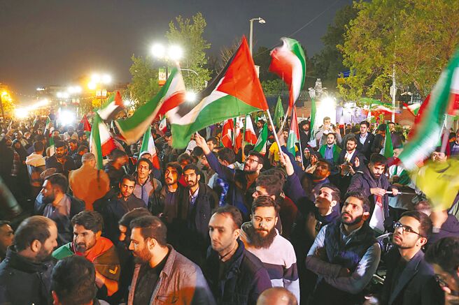 伊朗14日對以色列發動襲擊後，示威者聚集在英國駐德黑蘭大使館前，激動揮舞伊朗國旗。（路透）