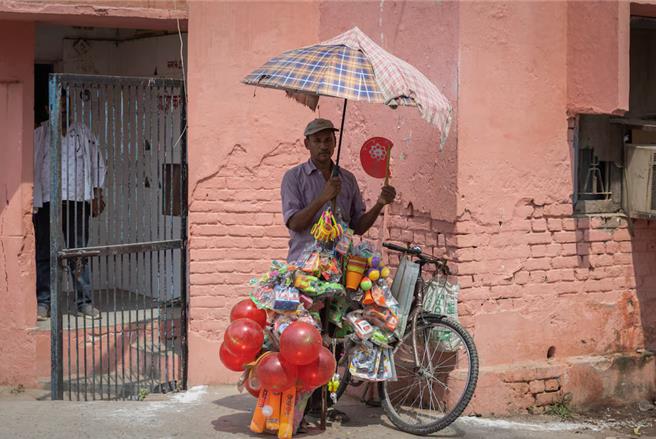 在伞下暂时避暑的印度街头小贩。（图／路透社）