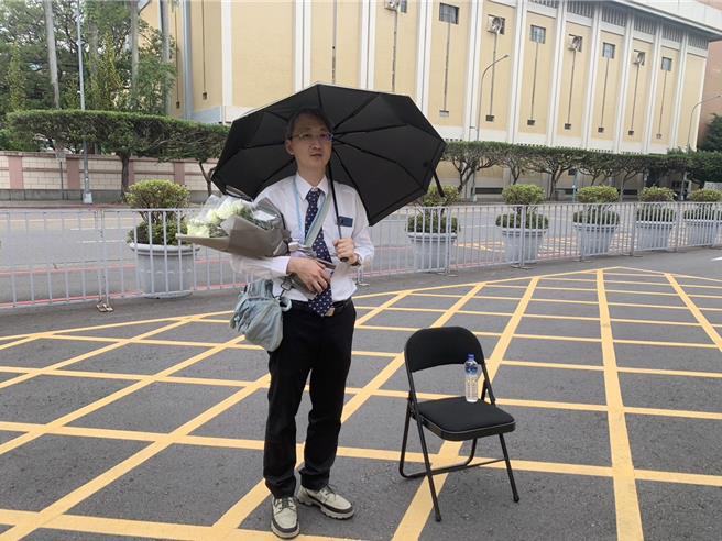 基隆地院法官李岳为表达对日前士林地院法官李昭然坠楼离世的哀悼，今天上午7时许拿着一束白玫瑰花并撑着黑伞，站在司法院正门口致意。（图赖佩璇摄）