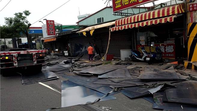1輛曳引車14日中午行經台中市霧峰區林森路943號前路段，載運的鋼板竟噴出散落一地，波及路旁2部重機車及商家招牌與鐵門損壞，現場一片狼藉。（民眾提供／潘虹恩台中傳真）
