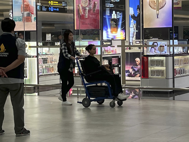 接受新航安排搭乘支援班机的旅客22日清晨抵达新加坡，有乘客乘坐轮椅在机场移动。（美联社）