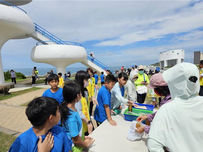 从盆栽草莓到开心农场，风柜国小师生卖起菜了。图为31日，学生在着名景点风柜洞前卖菜，国泰慈善基金会还派人（黄色背心者）前来观看这场成果发表。（风柜国小提供／许逸民澎湖传真）