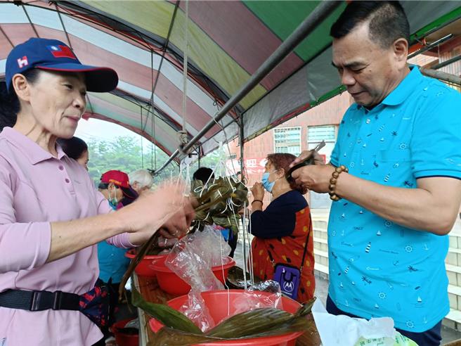 埔心社區舉辦親子包肉粽活動，吸引超過百位民眾齊聚社區活動中心前，一起包肉粽；埔心村長邱芳春（左）、社區發展協會理事長許增鏞（右）也一起體驗包肉粽的樂趣。（葉靜美攝）