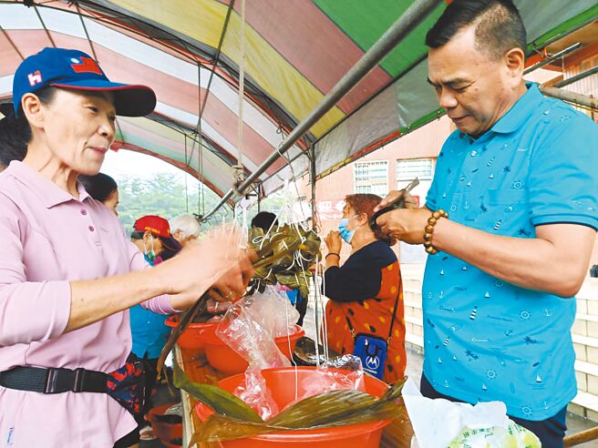 彰化縣埔心社區舉辦親子包肉粽活動，吸引超過百位民眾齊聚社區活動中心前，一起包肉粽；埔心村長邱芳春（左）、社區發展協會理事長許增鏞（右）也一起體驗包肉粽的樂趣。（葉靜美攝）