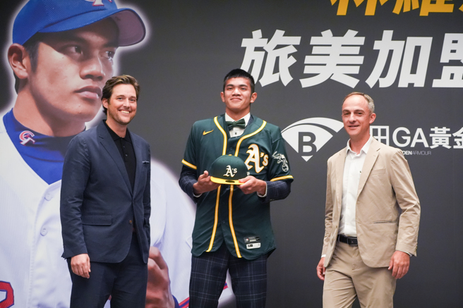 平鎮高中好手林維恩（中）加盟運動家隊，國際球探部門總監夏普（Steve Sharpe，左）與球探希斯洛普（Adam Hislop）為他披上球帽、球衣。（大漢運動行銷提供）