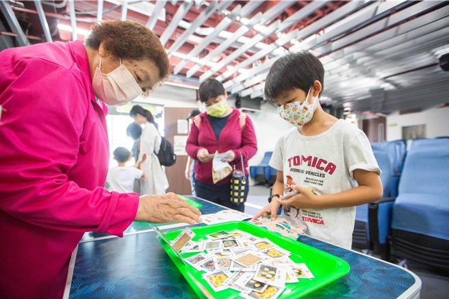 民眾拿起粽型布包、挑選裝入合適的食材小卡，若選到錯誤的食材，志工現場會即時指導修正。（袁庭堯攝）